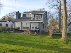 A two-story house with a balcony, large windows, and a grassy yard. - Baseline Lakefront - Beautiful views, shallow swimming area - Huron chain with 7 lakes (Pinckney)