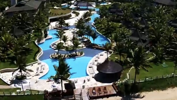 Un resort con piscina central, rodeado de palmeras y zonas de descanso.