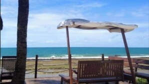 Vista de la playa con una palmera, un banco de madera y una sombrilla de metal.