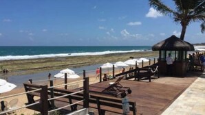 Una terraza frente al mar con barandas de madera, una estructura de techo de paja y sombrillas de playa.
