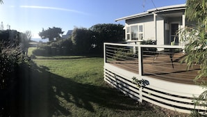 A house with a deck, surrounded by greenery and a clear sky.