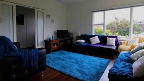 A living room with a blue rug, a sofa, a television, and a window with a view of greenery.