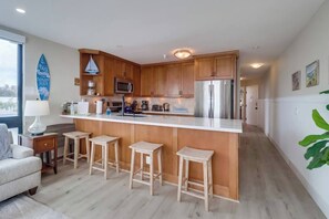 Eine moderne Küche mit Holzschränken, einer zentralen Kochinsel mit Hockern, Edelstahlgeräten und Blick ins Freie.