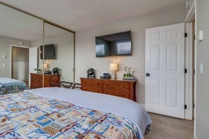 A hotel room with a large bed, a dresser, a mirror, a flat-screen TV, and a door.