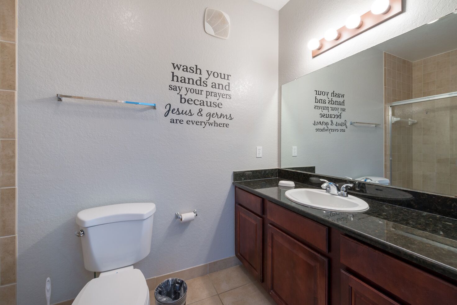 Une salle de bain équipée de toilettes, d’un lavabo, d’un meuble-lavabo et d’un miroir avec éclairage. Les murs sont décorés d’autocollants avec des messages inspirants.
