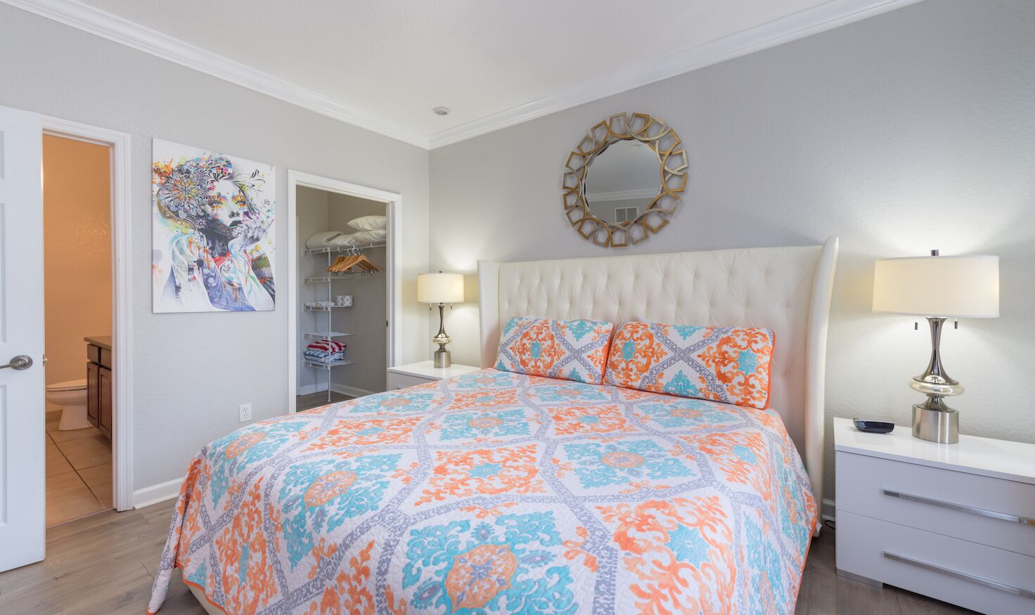 Een slaapkamer met een groot bed, een nachtkastje met een lamp, een kledingkast en een spiegel aan de muur.