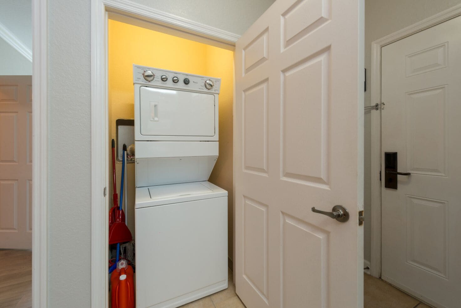 A laundry room with a stacked washer and dryer, a mop, and cleaning supplies.