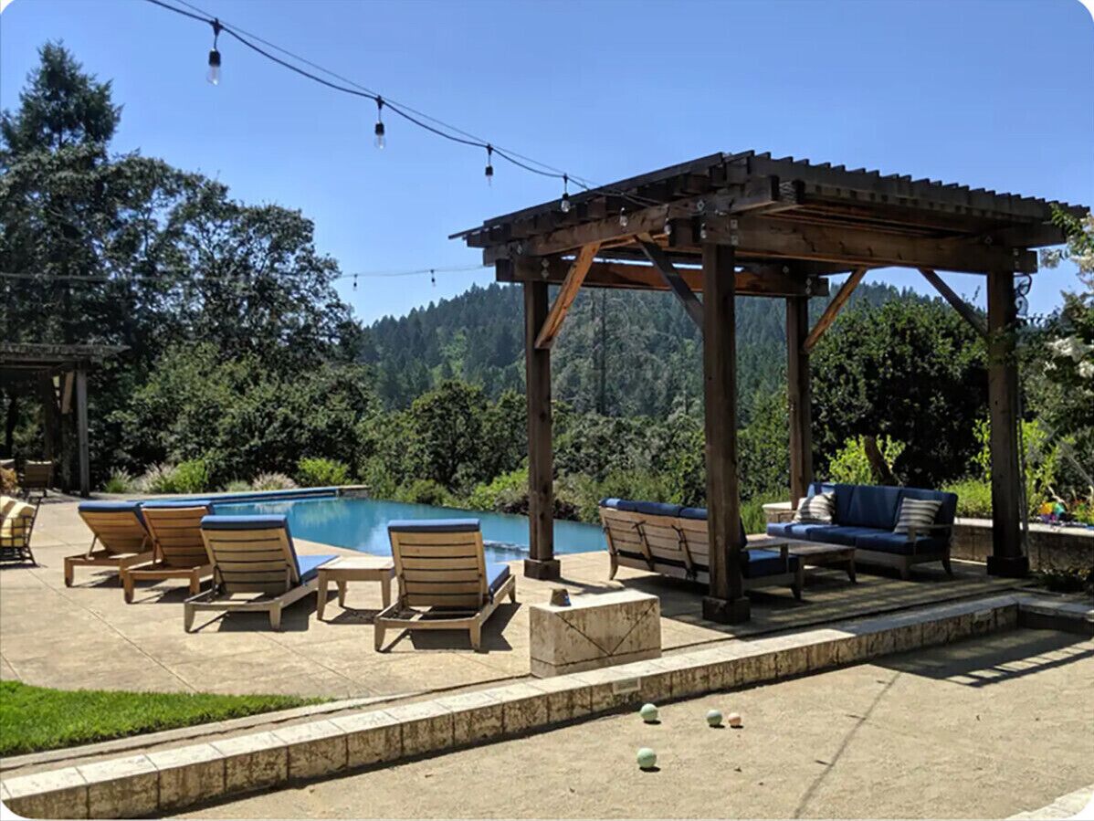 Ein Poolbereich mit Liegestühlen, einer Holzpergola und Blick auf eine Berglandschaft.