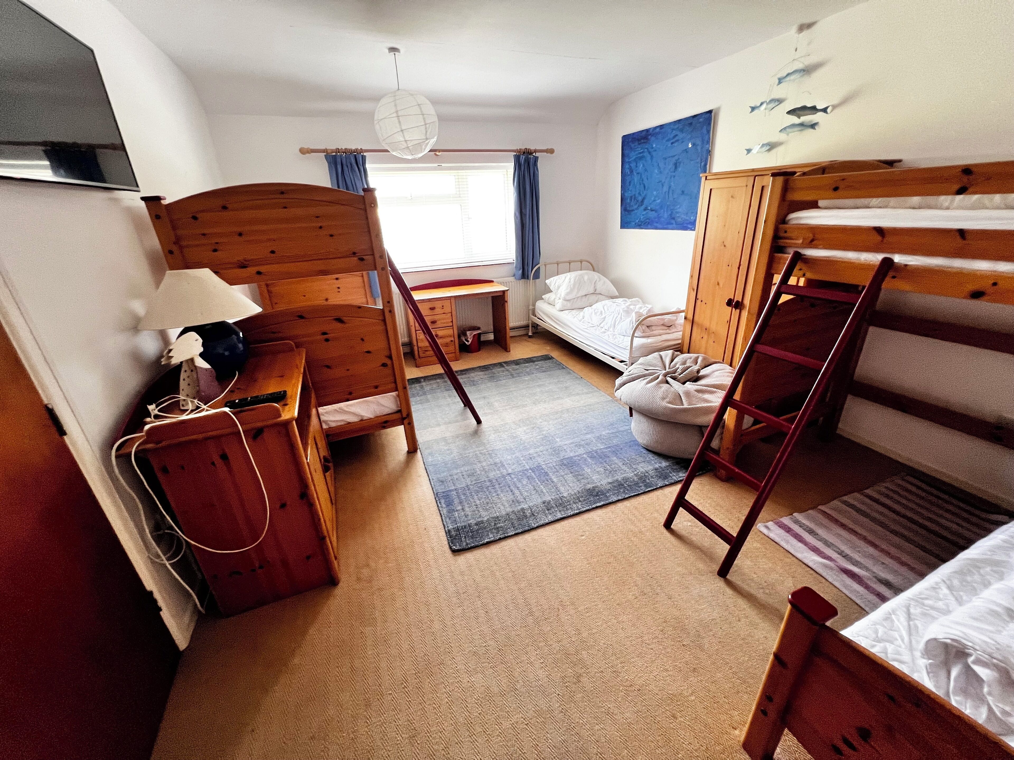 A compact room with a bunk bed, a desk with a chair, a small table, and a window with curtains.