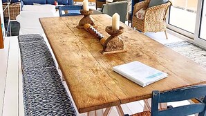 Un vaste espace de vie comprenant une table à manger en bois, un banc à motifs bleus et des chaises en osier.