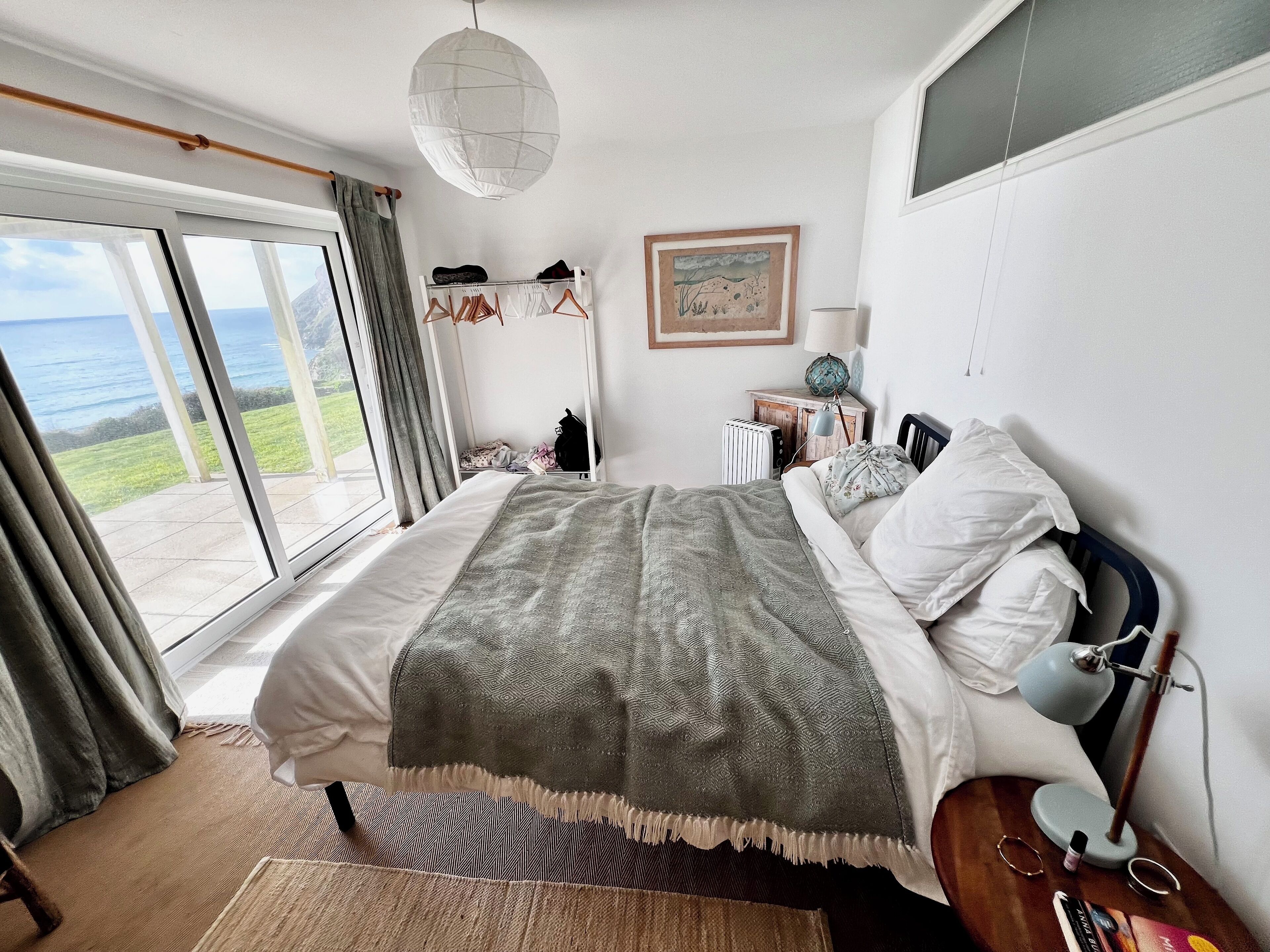 Une chambre avec un grand lit, une vue sur la mer, une commode et une lampe.