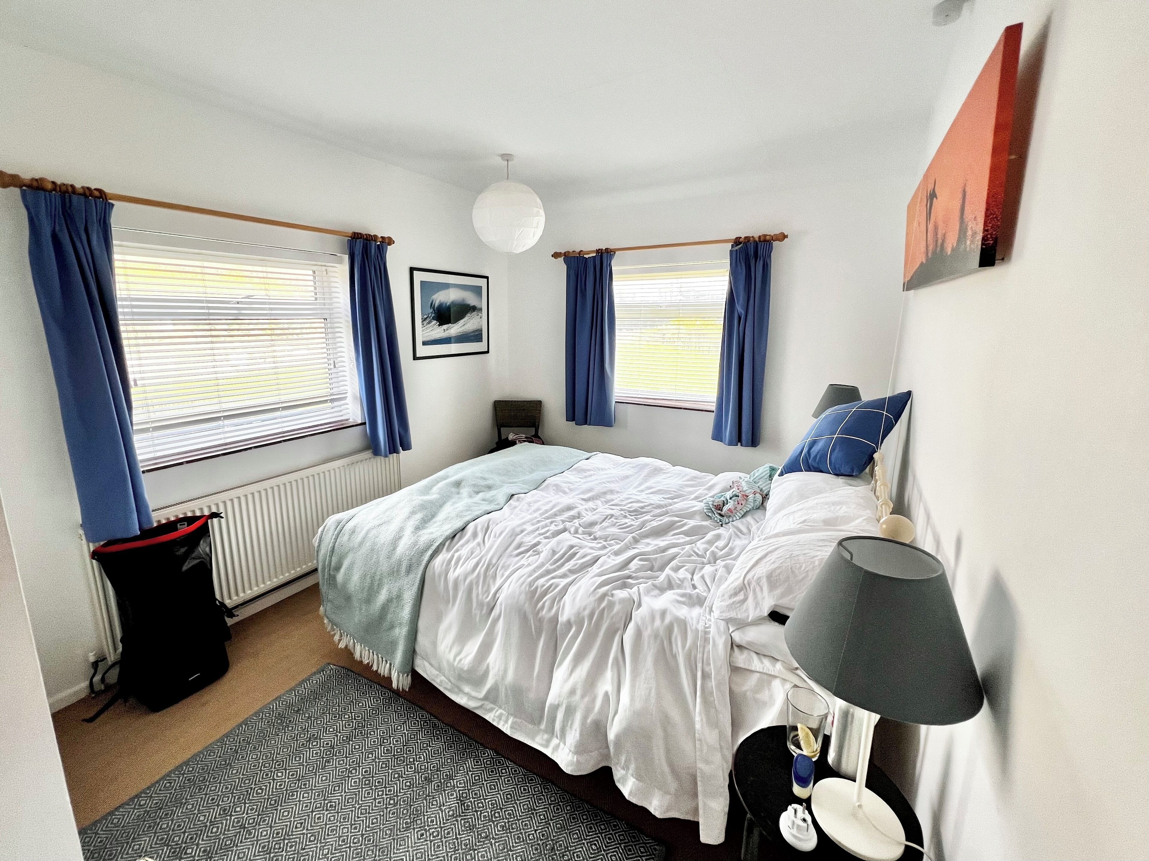 A bedroom with a bed, a bedside table with a lamp, a radiator, and a window with curtains.