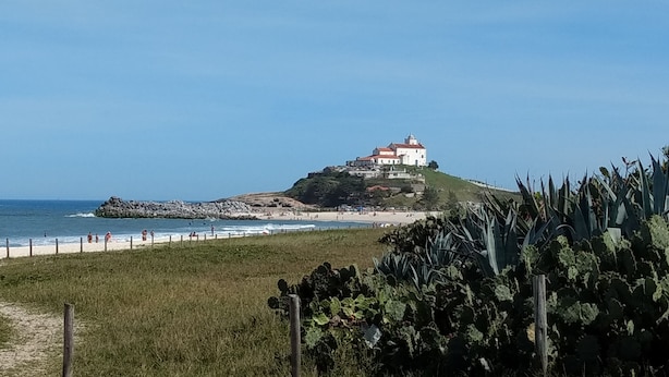 Un edificio costiero con un faro su una collina, affacciato sulla spiaggia e l'oceano.