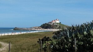 A coastal building with a lighthouse on a hill, overlooking the beach and ocean.