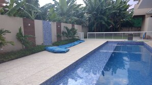 Una piscina con bordo piastrellato, scala in metallo e recinzione bianca.