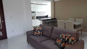 Un soggiorno moderno con divano e cuscini coordinati, una zona pranzo con tavolo e sedie, e una cucina sullo sfondo.