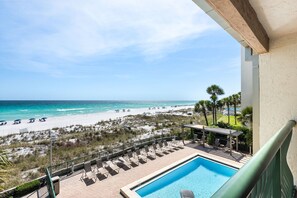 A pool area with lounge chairs, a view of the beach, and a clear sky.