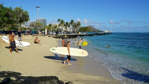 Une plage où l’on voit des gens se promener et faire de la planche à voile, un ciel dégagé et une montagne lointaine.