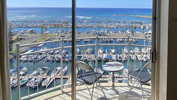 Un balcon offrant une vue sur une marina où sont amarrés de nombreux bateaux, avec un ciel bleu dégagé.