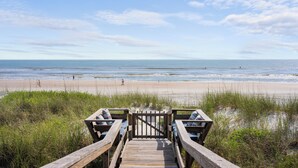 Ein hölzerner Steg führt zu einem Strand mit Blick aufs Meer.