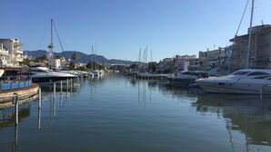 Un port de plaisance avec des bateaux amarrés, des bâtiments en arrière-plan et des montagnes à l’horizon.