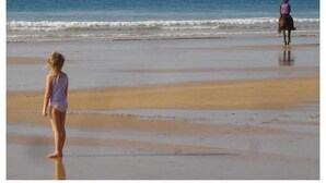 Una spiaggia con una persona in piedi e un'altra a cavallo in lontananza.