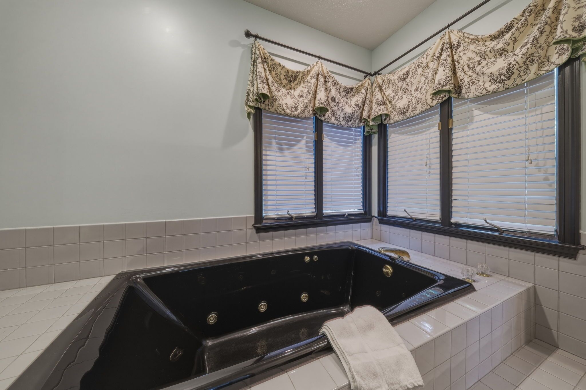 Un baño con una bañera negra, paredes cubiertas de azulejos blancos y una ventana con persianas.