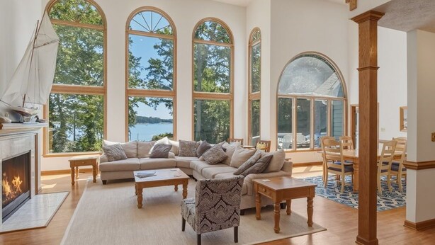 A spacious living room with a fireplace, large arched windows, and a wooden staircase. - Waterfront Retreat w/ Pool, Hot Tub, Dock & Sand Beach. Relax & enjoy the Rivah! (Lancaster)