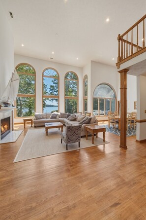 A spacious living room with a fireplace, large arched windows, and a wooden staircase. - Waterfront Retreat w/ Pool, Hot Tub, Dock & Sand Beach. Relax & enjoy the Rivah! (Lancaster)