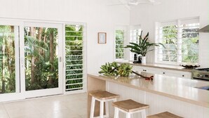 A spacious kitchen with white cabinetry, a central island with stools, and large windows with tropical views.
