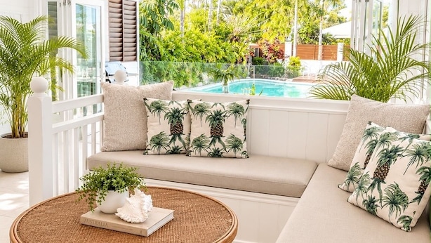A modern living room with a white sofa, round wicker coffee table, and a view of a pool and greenery outside.