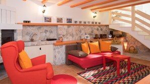 Un'accogliente zona living con camino in pietra, travi in legno, un divano rosso e un tappeto colorato.