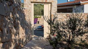 Un arco in pietra conduce a un'area esterna coperta con vista su un giardino e un edificio con tetto in tegole.