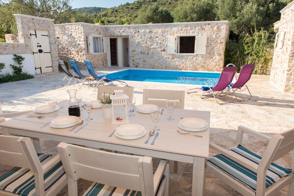 A stone villa with a pool, dining set, and lounge chairs.