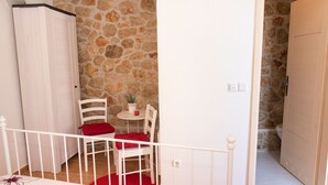 Una stanza con un muro in pietra, un armadio bianco, un tavolino con un cuscino rosso e una sedia bianca.