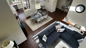 Un salon moderne avec un canapé bleu foncé, un coin repas avec des tables rondes et une cuisine visible à travers une porte ouverte.