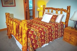 Ein Bett mit geometrischem Muster auf der Bettdecke, einem Holz-Kopfteil und einem Nachttisch mit Lampe.