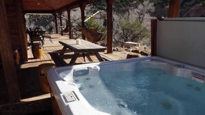 Een hottub met een houten terras, zitplaatsen buiten en uitzicht op het omliggende landschap.