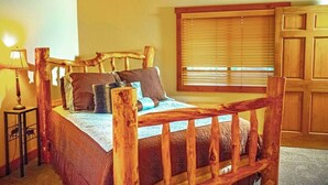 Een houten bed met hoofdbord, een nachtkastje met lamp en een raam met zonwering.