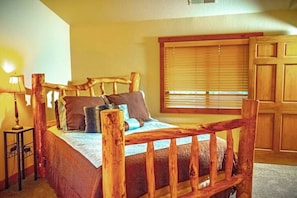 A wooden-framed bed with a headboard, a bedside table with a lamp, and a window with blinds.