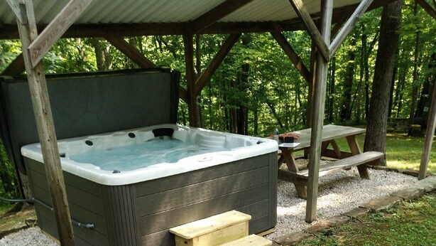 A hot tub under a wooden pergola with a stone pathway leading to it.