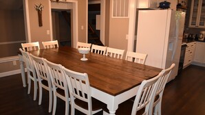 A dining area with a wooden table and white chairs, a white refrigerator, and a kitchen area with cabinets and appliances.