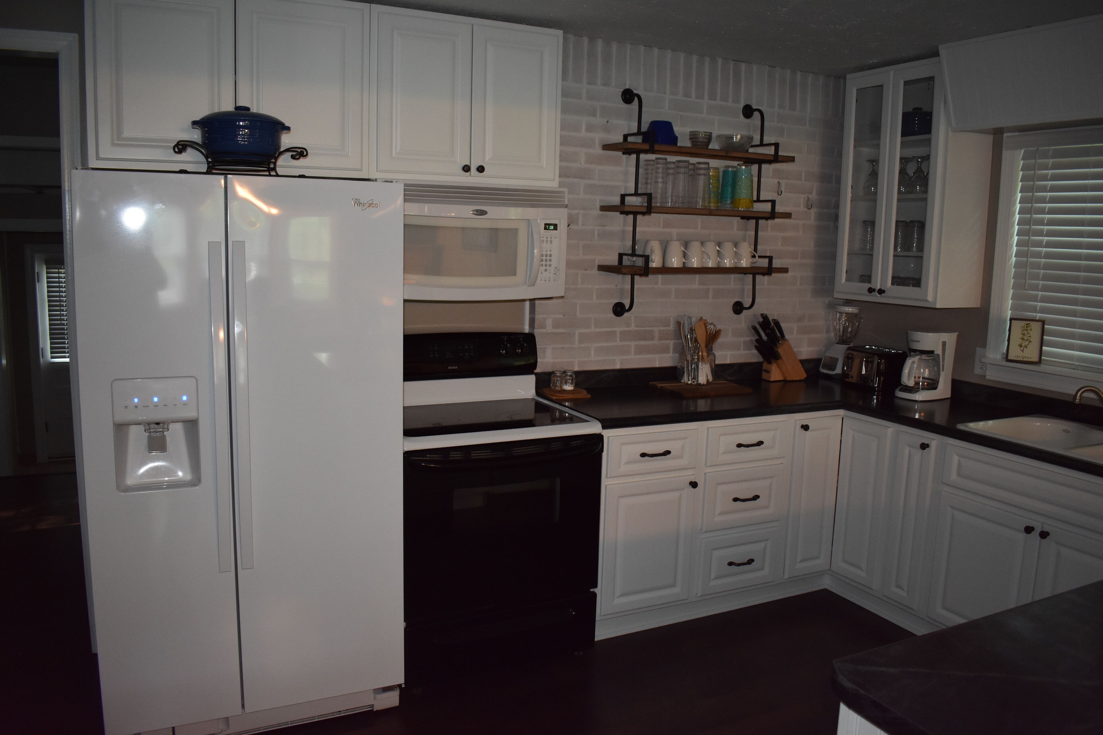 A kitchen with white cabinets, a microwave, a stove, a water dispenser, and a coffee maker.