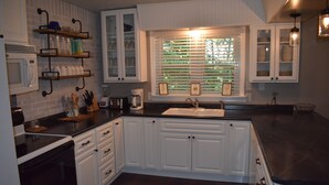 A kitchen with white cabinets, a black countertop, a sink, and a window with blinds.