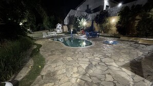 Un patio de piedra con piscina, sillas de descanso y un pequeño edificio.