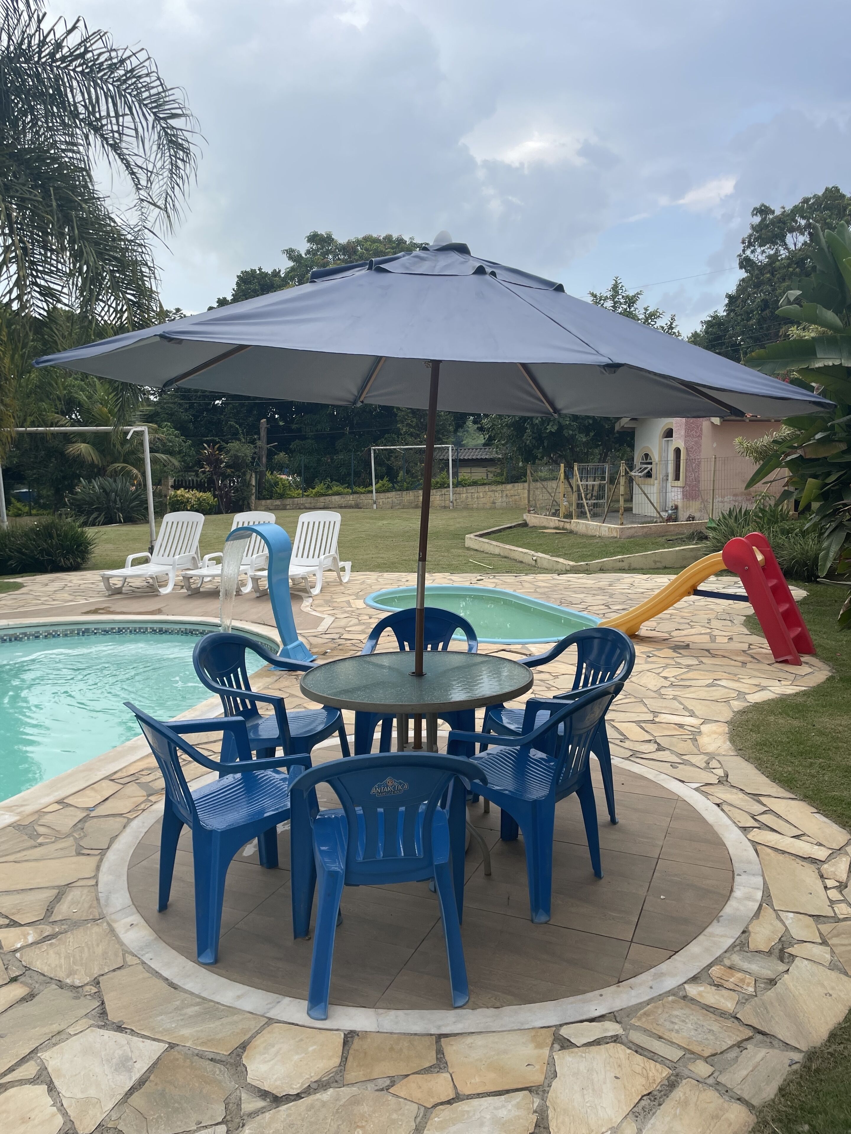 Un espace piscine comprenant une table et des chaises, un toboggan et un coin salon abrité.