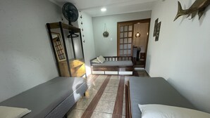 Una habitación con dos camas individuales, un aparador de madera, un ventilador y una puerta que da a otra estancia.