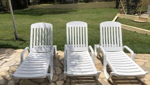 Tres sillones blancos en un patio de piedra con un césped al fondo.