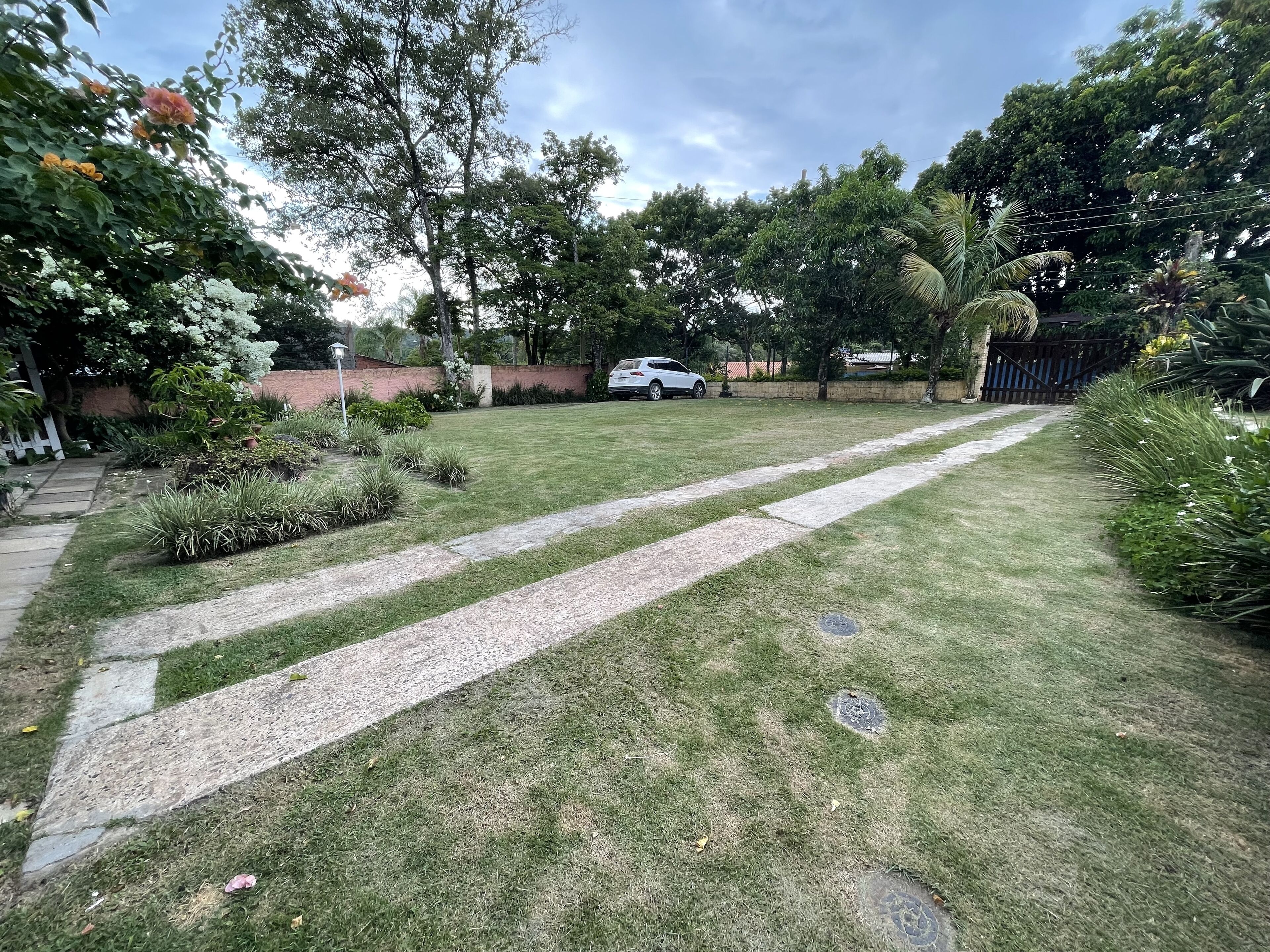 Un jardin bien entretenu, avec un chemin pavé, une végétation luxuriante et une voiture garée.