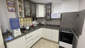 Una cocina compacta con gabinetes blancos, un microondas integrado, una estufa a gas y un dispensador de agua.